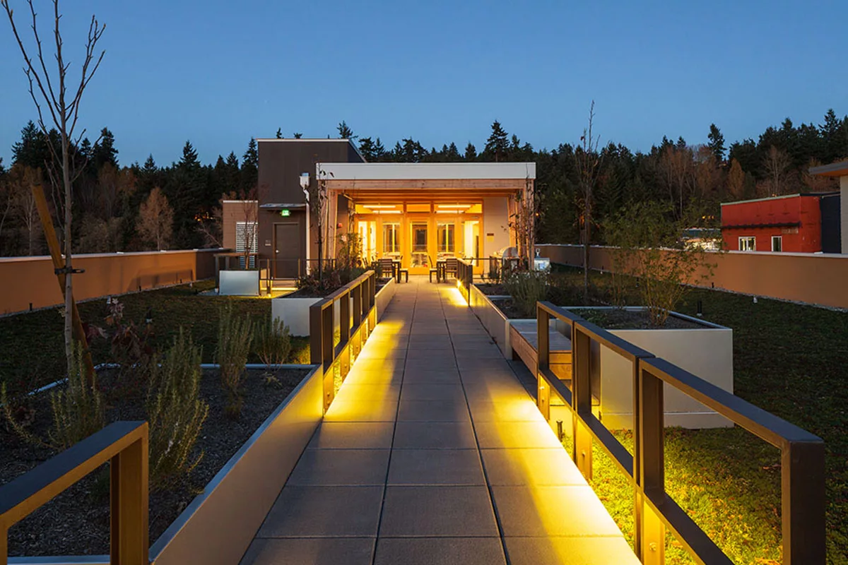 A dimly-lit rooftop walkway surrounded by planters and green roof modules.